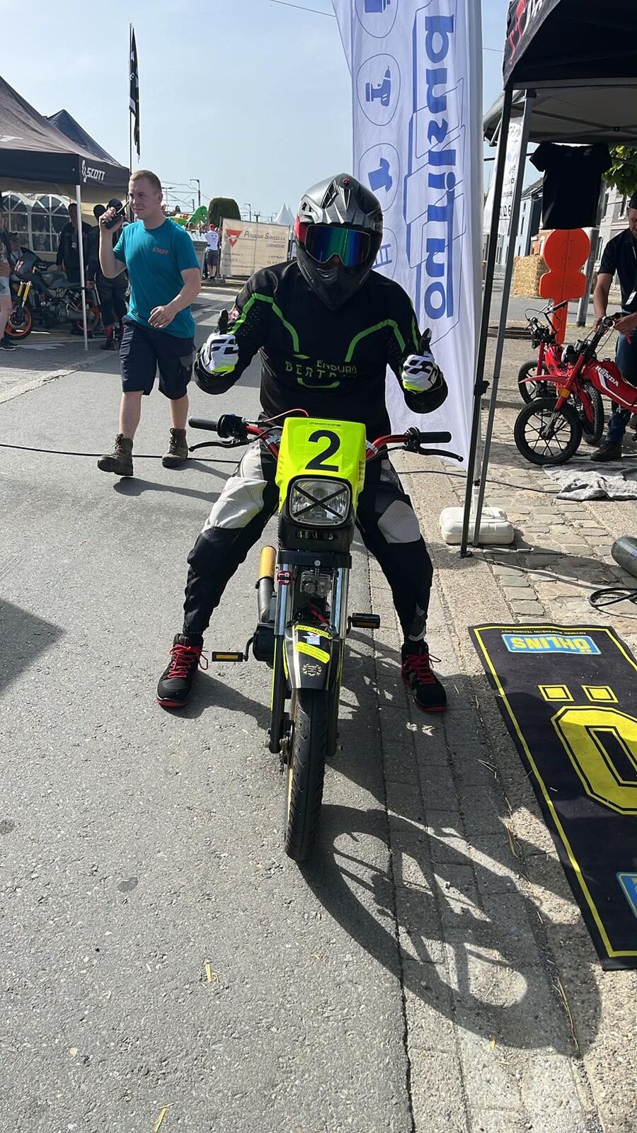 Étienne casqué, assis sur la n°2 devant le stand